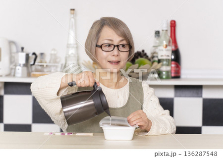 キッチンでカップ麺にお湯を入れるシニア女性 キッチンでカップ麺にお湯を入れるシニア女性 136287548
