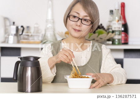 キッチンでカップ麺にお湯を入れるシニア女性 136287571