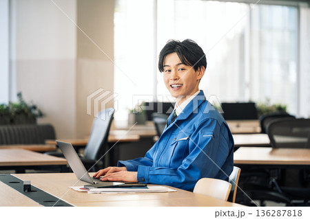 オフィスでデスクワークをする作業服姿の若い男性 オフィスでデスクワークをする作業服姿の若い男性 136287818