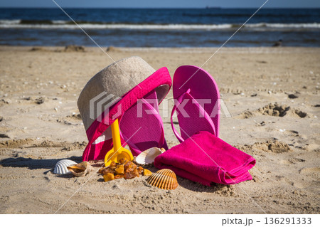 Accessories for relax on sand. Straw hat, slippers and towel. Summer time on beach Accessories for relax on sand. Straw hat, slippers and towel. Summer time on beach 136291333