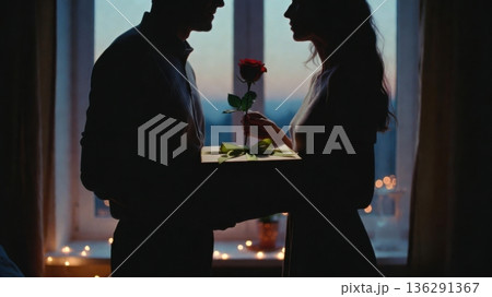 Silhouette couple exchanging rose and gift by window at dusk 136291367