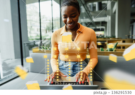 Woman uses laptop in office with digital elements floating around 136291530