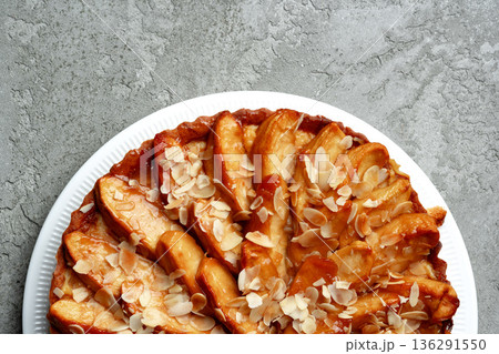Delicious baked apple tart with almond slices on white plate against gray background Delicious baked apple tart with almond slices on white plate against gray background 136291550