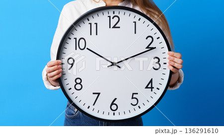 Holding a large clock showing the time and a blue background Holding a large clock showing the time and a blue background 136291610