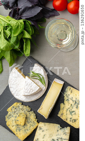 Cheese platter with greens, tomatoes, and glass of white wine on a table 136291650