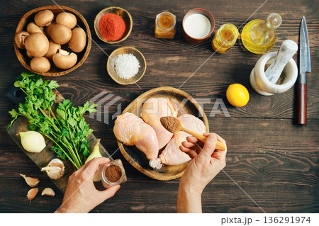 Hands seasoning raw chicken legs with spice on rustic wooden table with ingredients Hands seasoning raw chicken legs with spice on rustic wooden table with ingredients 136291974