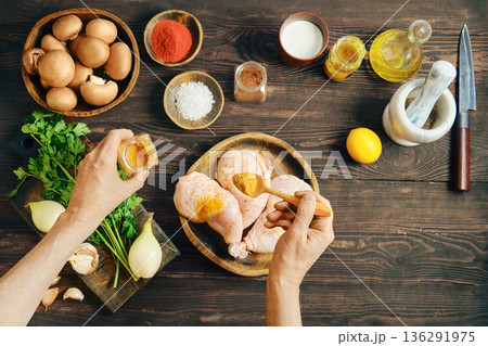 Hands seasoning raw chicken legs with curry on wooden tabletop with ingredients 136291975
