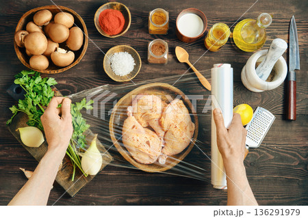 Hands wrapping marinated chicken with plastic stretch film for marinating or storage 136291979