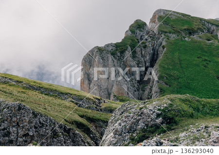 Mountain cliffs covered with green grass rising above clouds in a dramatic alpine landscape. Mountain cliffs covered with green grass rising above clouds in a dramatic alpine landscape. 136293040