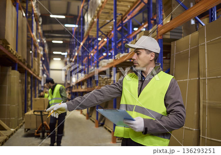 Warehouse logistics worker directing loading while checking inventory on shelves 136293251