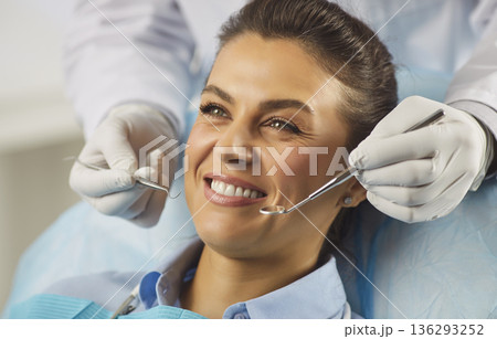Happy patient at dental clinic receiving routine checkup with mirror and scaler 136293252