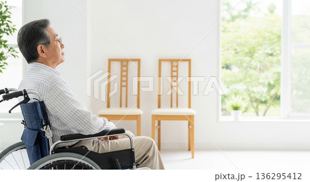 車椅子で明るい窓辺を眺めるシニア男性の後ろ姿。介護施設や自宅での穏やかで安心感のある老後のイメージ。 136295412