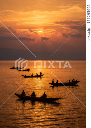 The serene waters of Lake Victoria at sunset, with traditional fishing boats silhouetted against a golden sky, depicting peaceful daily life. The serene waters of Lake Victoria at sunset, with traditional fishing boats silhouetted against a golden sky, depicting peaceful daily life. 136295993