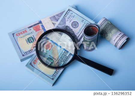 Magnifying glass inspecting us dollar bills on blue background 136296352