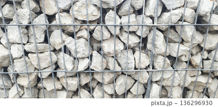 Close-up texture shot of a gabion wall, showing light gray, rough-cut stones tightly packed within a gray wire mesh cage Close-up texture shot of a gabion wall, showing light gray, rough-cut stones tightly packed within a gray wire mesh cage 136296930