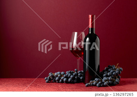 Bottle and glass of red wine with blue grapes on a red background. Bottle and glass of red wine with blue grapes on a red background. 136297265