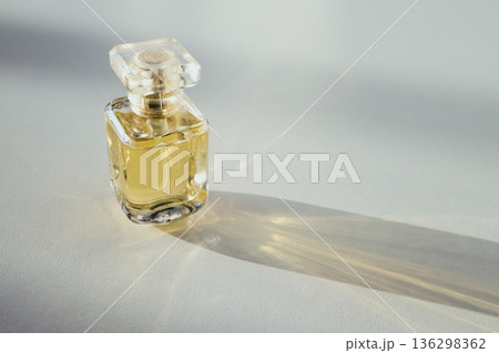 Glass perfume bottle with yellow liquid and long shadow on white surface Glass perfume bottle with yellow liquid and long shadow on white surface 136298362