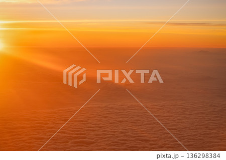 A bright sunset shows warm colors mixing with clouds in the sky. Light spills over the horizon creating a warm scene. This is a view from an airplane high above the ground. High quality photo A bright sunset shows warm colors mixing with clouds in the sky. Light spills over the horizon creating a warm scene. This is a view from an airplane high above the ground. High quality photo 136298384