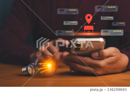 Person using smartphone with glowing local store icons, map pin, and star ratings, symbolizing online business reviews, location search, local SEO, and digital marketing for small businesses. 136299693