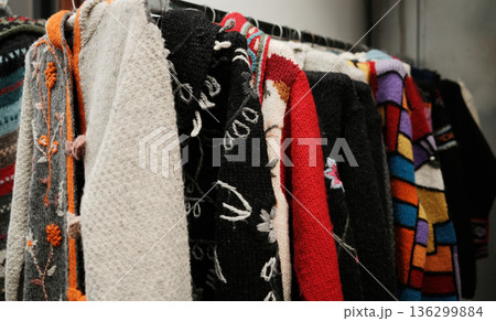 Close-up of handmade knitted sweaters and scarves hanging on a rack, showing rich textures, colorful yarn, and traditional patterns, emphasizing warmth, craft quality, and winter fashion detail Close-up of handmade knitted sweaters and scarves hanging on a rack, showing rich textures, colorful yarn, and traditional patterns, emphasizing warmth, craft quality, and winter fashion detail 136299884