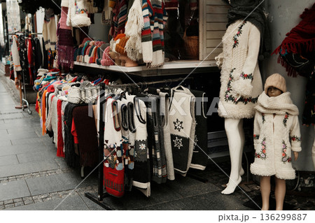 Street market stall displaying handmade knitted sweaters, scarves, and vests with folk patterns, presented on mannequins and racks, reflecting traditional winter fashion and local craft culture Street market stall displaying handmade knitted sweaters, scarves, and vests with folk patterns, presented on mannequins and racks, reflecting traditional winter fashion and local craft culture 136299887
