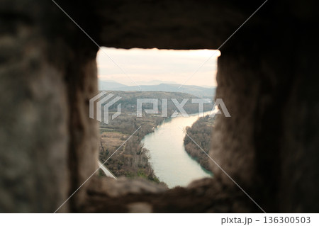 View through a stone window of Pocitelj Fortress overlooking the winding Neretva River and quiet valley landscape in southern Bosnia and Herzegovina View through a stone window of Pocitelj Fortress overlooking the winding Neretva River and quiet valley landscape in southern Bosnia and Herzegovina 136300503