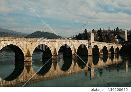 Historic Mehmed Pasha Sokolovic Bridge spans the Drina River in Visegrad, Bosnia and Herzegovina. Stone arches and soft reflections highlight the calm atmosphere of this iconic landmark Historic Mehmed Pasha Sokolovic Bridge spans the Drina River in Visegrad, Bosnia and Herzegovina. Stone arches and soft reflections highlight the calm atmosphere of this iconic landmark 136300626