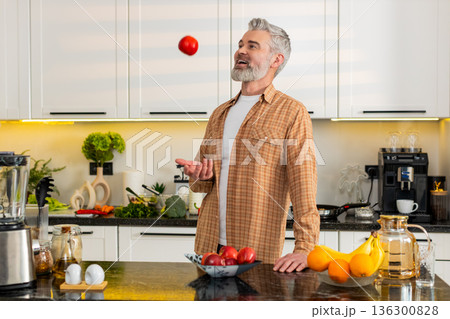 Middle-aged man bites fresh apple in kitchen for healthy diet snack smiling satisfied home kitchen 136300828