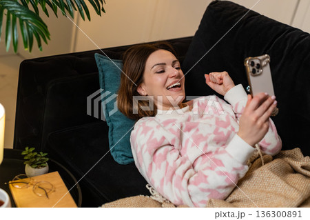 Adult woman lying down at night gets smartphone jackpot win notification smiles raises victory hand 136300891