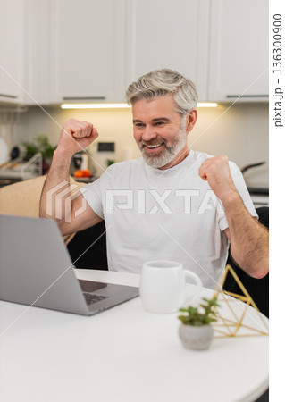 Middle-aged man celebrates discount and promo code success on laptop cheers for jackpot lottery win Middle-aged man celebrates discount and promo code success on laptop cheers for jackpot lottery win 136300900