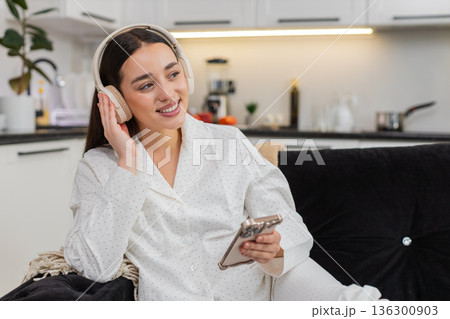 Young woman in wireless headphones listens to music with smartphone relax closed eyes chill zen mood Young woman in wireless headphones listens to music with smartphone relax closed eyes chill zen mood 136300903