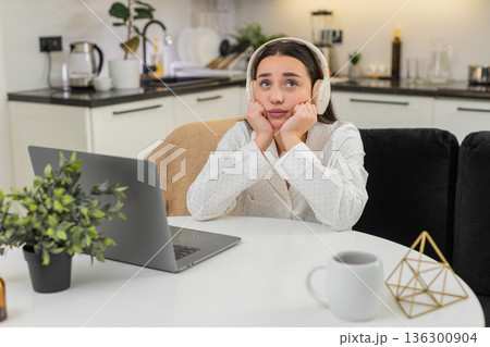 Young woman in headphones thinking with laptop leans on hands worried decision responsibility mind 136300904