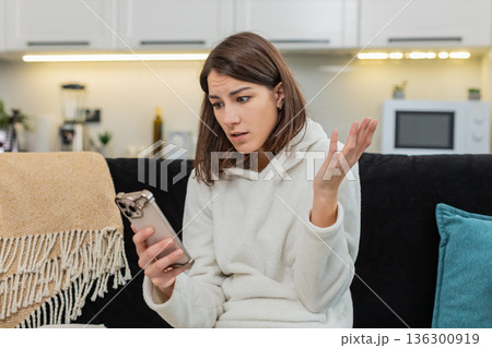 Young woman upset by negative alert on smartphone frowns whispers very anxious stress worried mood Young woman upset by negative alert on smartphone frowns whispers very anxious stress worried mood 136300919