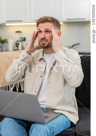 Young man with laptop suffers headache rubs temples closes eyes takes breath long break relief calm 136300926