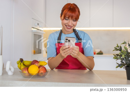 Young woman in apron at bar uses smartphone sees good news smiles celebrates win with happy bounce Young woman in apron at bar uses smartphone sees good news smiles celebrates win with happy bounce 136300950