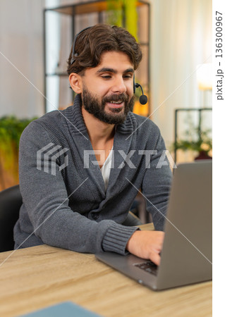 Indian man in headset at laptop friendly support agent listens writes key points customer care calm 136300967