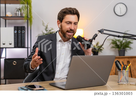 Middle-aged businessman records vlog on laptop with studio mic telling funny jokes expressively now 136301003