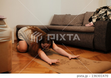 A woman stretches forward on a yoga mat in a child s pose, creating a calm moment of relaxation and flexibility during her home routine A woman stretches forward on a yoga mat in a child s pose, creating a calm moment of relaxation and flexibility during her home routine 136301470