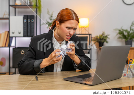 Young businesswoman reacts to report mismatch on laptop crushes paper angrily and fears audit ahead 136301572