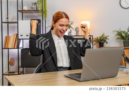 Young businesswoman celebrates project approval on laptop breathes loudly shouting victory success Young businesswoman celebrates project approval on laptop breathes loudly shouting victory success 136301573
