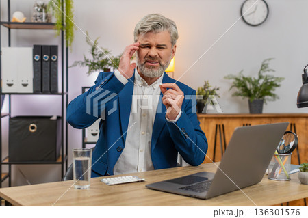 Middle-aged businessman massages temples swallows headache pill drinks water again to return to work 136301576