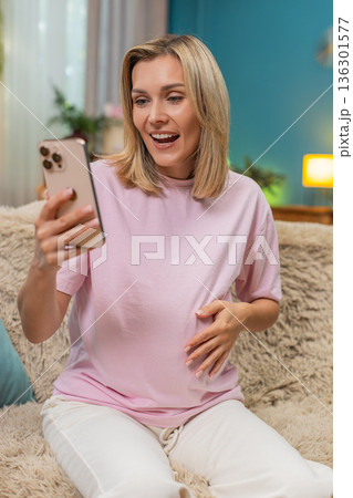 Pregnant woman celebrating baby news texting on smartphone making victory sign smiling super indoors 136301577