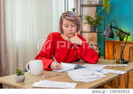 Woman carefully writing notes from financial documents, serious concentrated business working mood 136301632