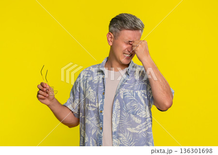 Adult man squinting eyes removing glasses rubbing face tired after long working time and eye strain Adult man squinting eyes removing glasses rubbing face tired after long working time and eye strain 136301698