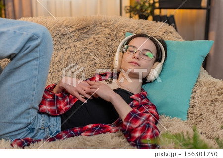 Woman listening to audiobook with wireless headphones at home, nodding with interest full attention 136301750