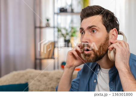 Man in headphones suddenly takes them off looking surprised reacting to strange unexpected sound Man in headphones suddenly takes them off looking surprised reacting to strange unexpected sound 136301800