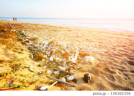 Trash on beach. People walk on sunset at sea. Garbage dump at ocean. Trash, debris on sea beach. Trash on beach. People walk on sunset at sea. Garbage dump at ocean. Trash, debris on sea beach. 136302356