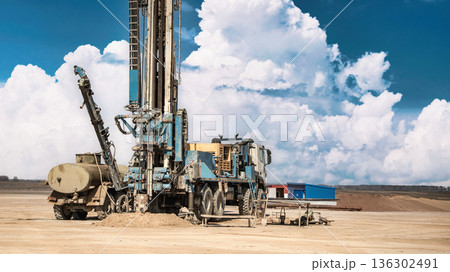 Drilling rig works on the ground to access oil and gas resources under clear skies with clouds in the background during daytime Drilling rig works on the ground to access oil and gas resources under clear skies with clouds in the background during daytime 136302491