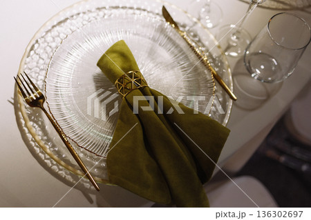 Green cloth napkin with gold ring on white glass plate on dark background 136302697