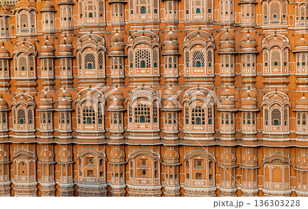 Detailed view of the pink sandstone facade of Hawa Mahal in Jaipur, India, with repeating arched windows and intricate lattice decoration. 136303228